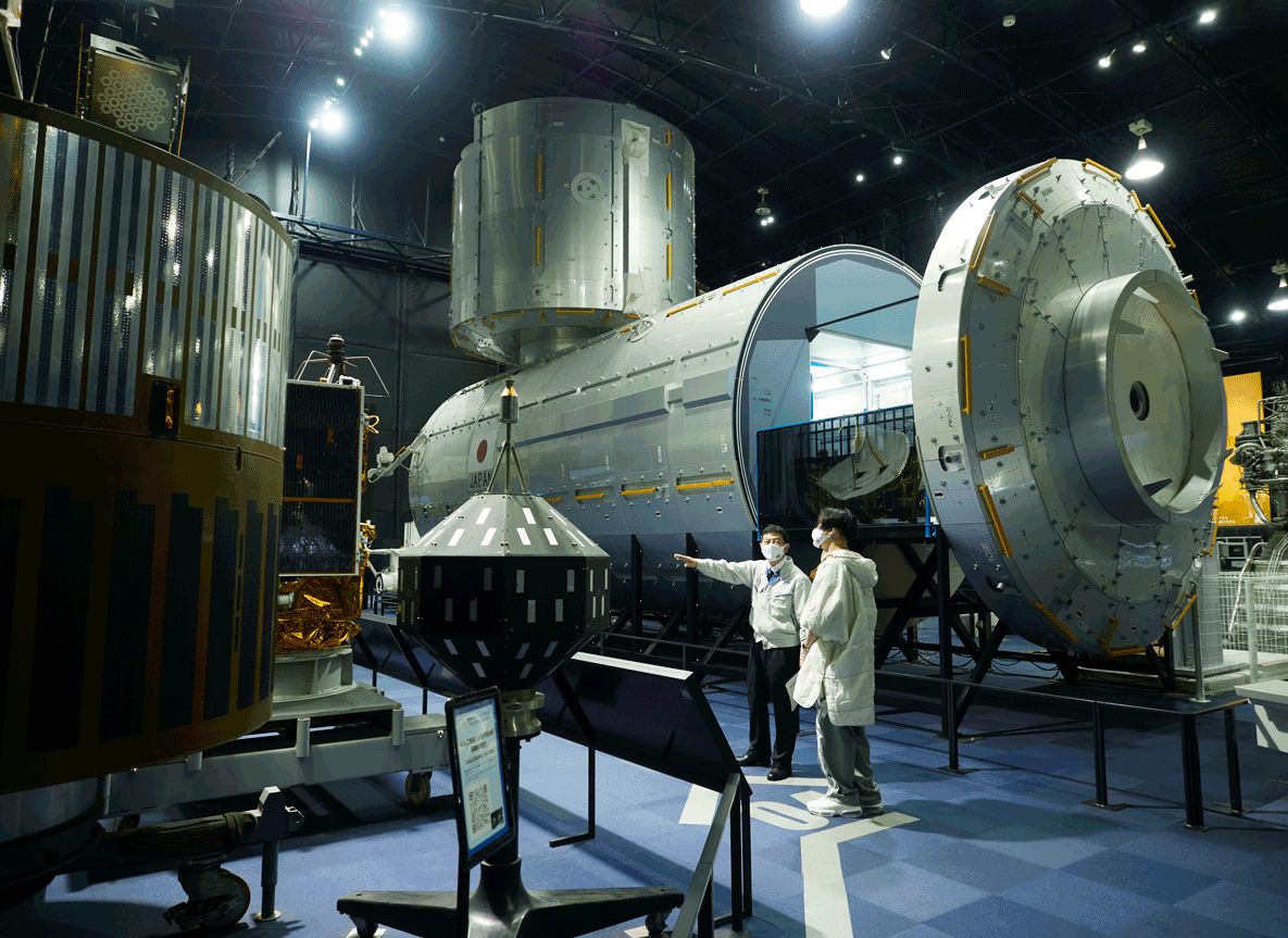 Guided by Center Director Terada, Mr. Kodama examines KIKU-1 at the Space Dome, an exhibition hall at the Tsukuba Space Center